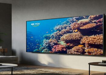 A modern living room with an Amazon Fire TV 4-Series mounted on the wall, displaying a vibrant underwater scene.