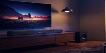 A sleek Polk Audio Signa S4 soundbar mounted beneath a TV, with a wireless subwoofer in the background, showcasing the system's design and audio performance.